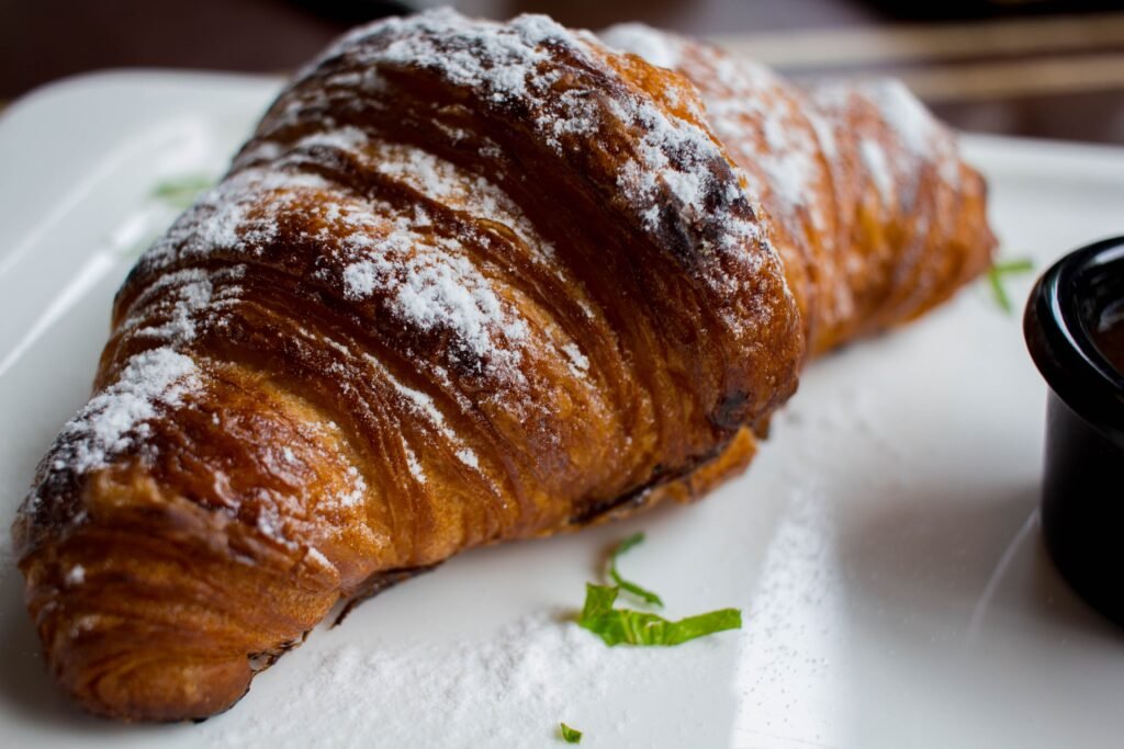 Freshly baked croissant dusted with powdered sugar, presented on a plate with mint garnish.